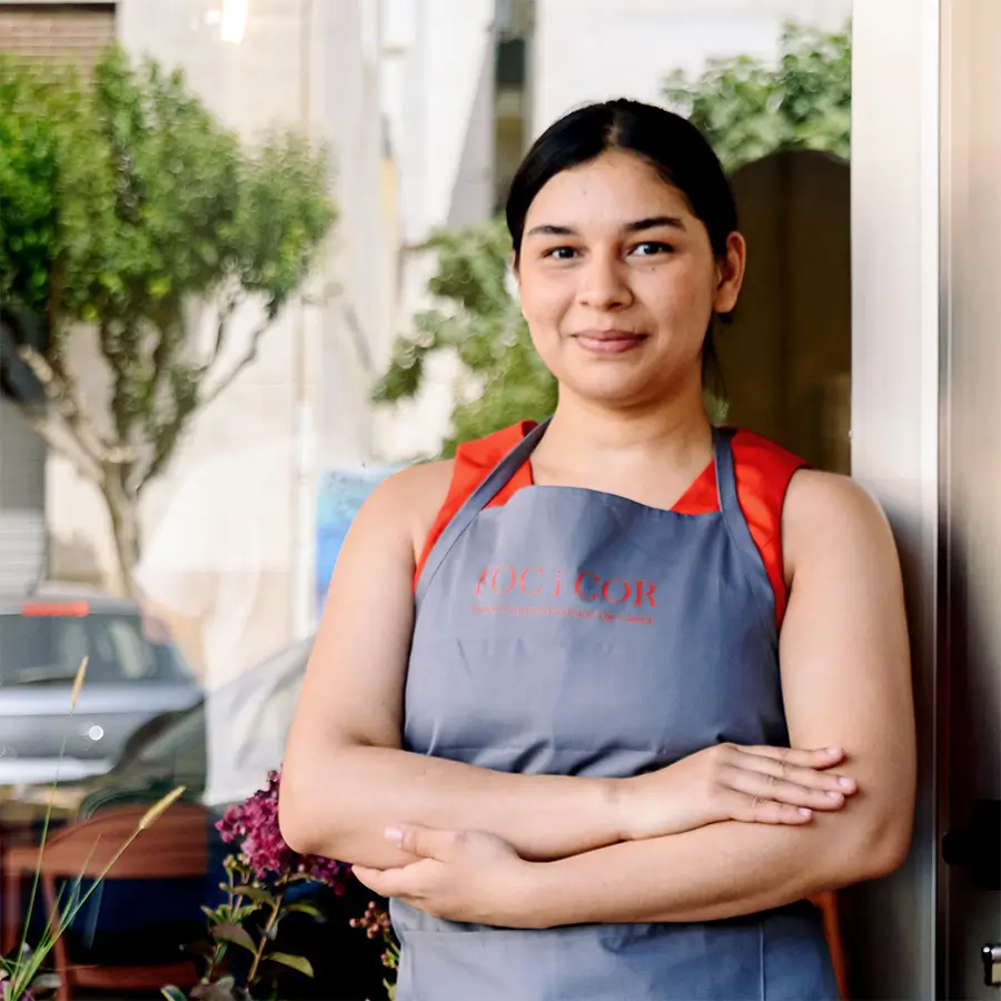 Una alumna del restaurant-escola, amb davantal, somriu a l'entrada del local